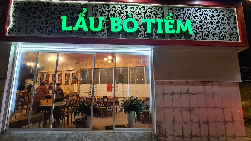 Bàn ăn dài bày đầy đĩa rau núi, bát nước chấm và nồi lẩu bò tiềm Yersin.